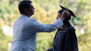 Father adjusts graduation cap on daughter's head.