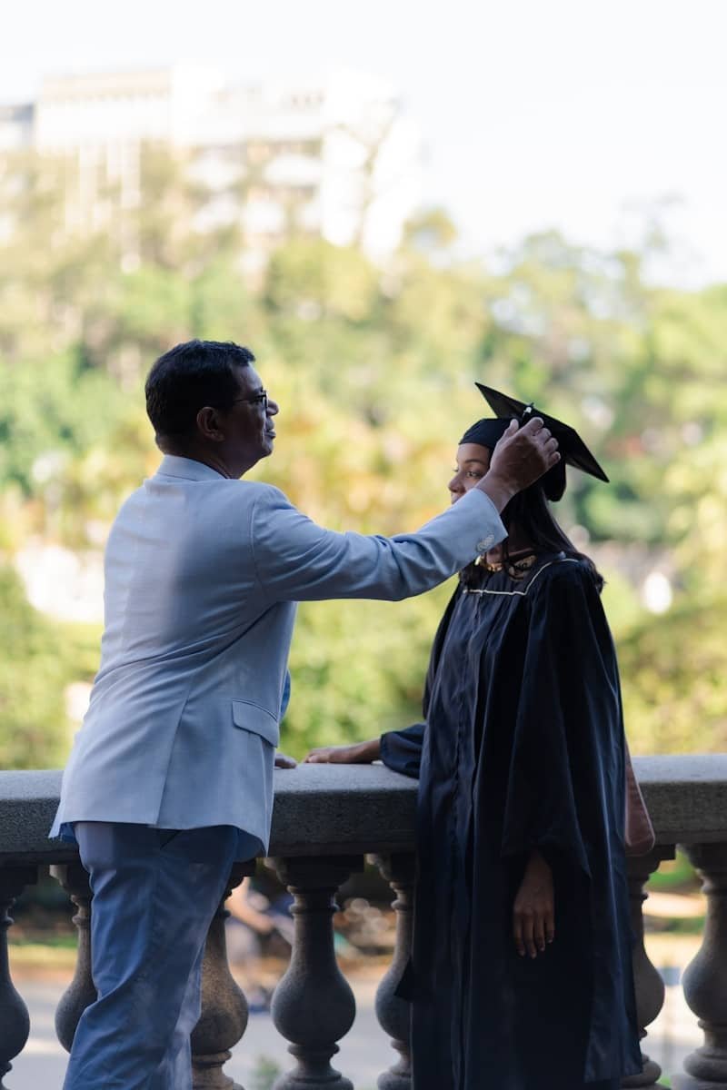 Father adjusts graduation cap on daughter's head.