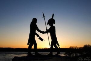Two figures shake hands at sunset by the water
