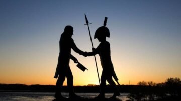 Two figures shake hands at sunset by the water