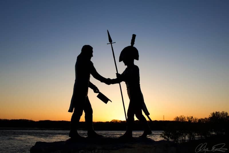 Two figures shake hands at sunset by the water